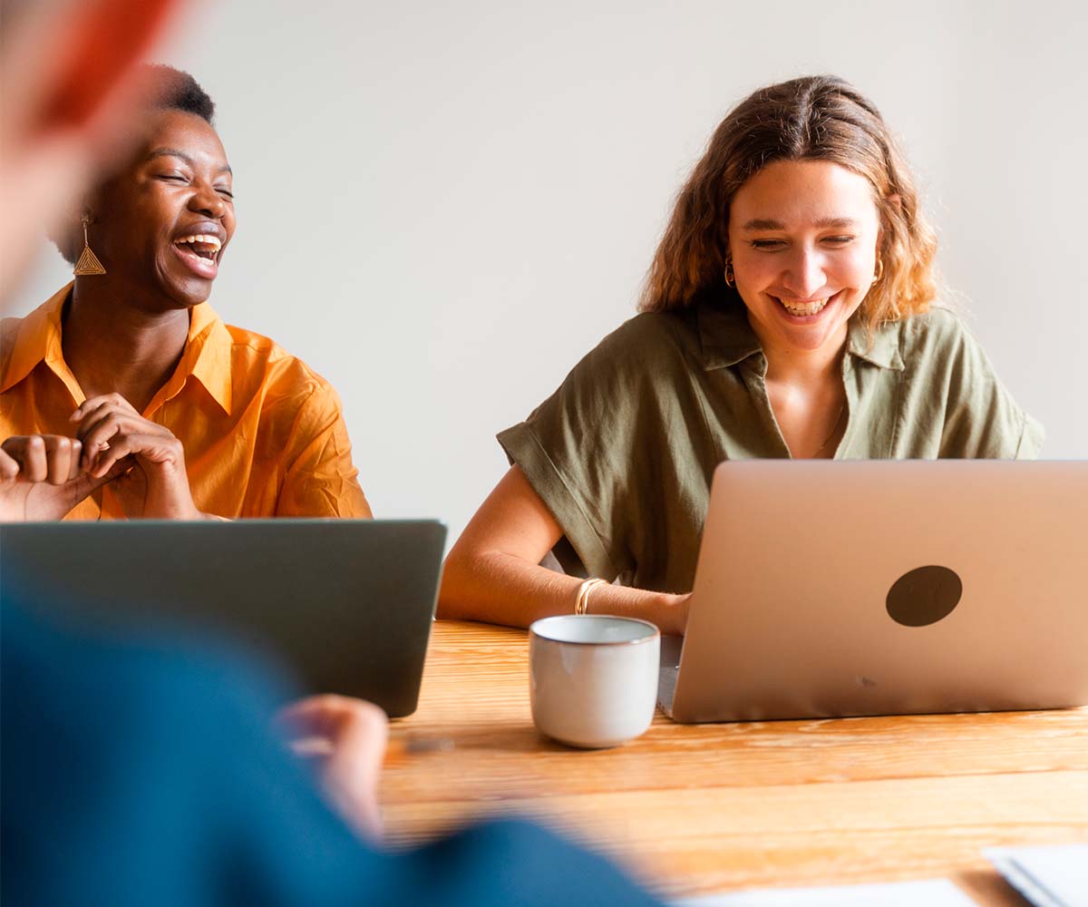 News Posting Graphic with a image of two women sitting at a office table at a meeting and looking at a laptop and laughing DIMOCO Payments